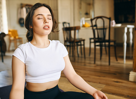 Beautiful young Caucasian woman with muscular curvy body sitting in lotus posture at home keeping eyes closed, meditating dur